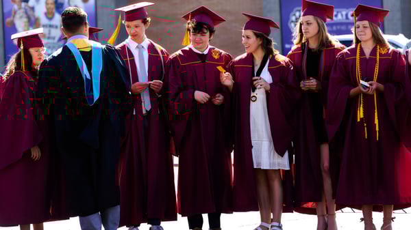 Absolventen der Utah Prep Academy in roten und schwarzen Talaren stehen zusammen vor unscharfem Stadtbild.