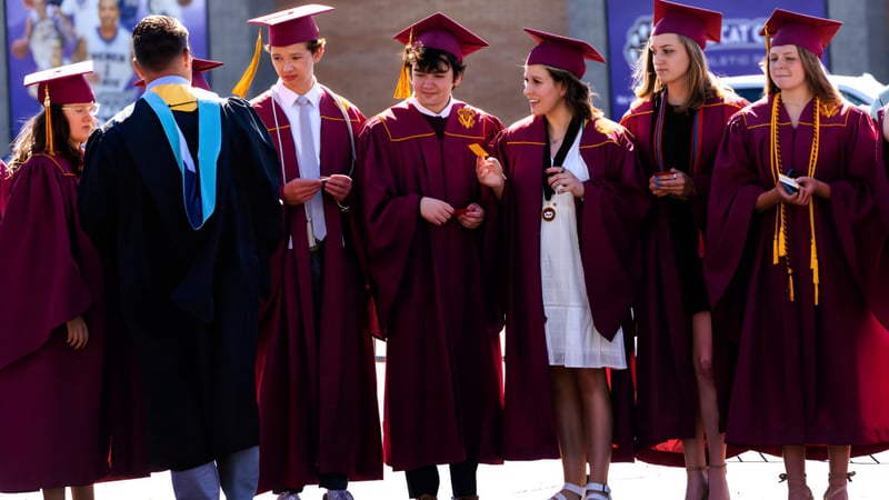 Absolventen der Utah Prep Academy in roten und schwarzen Talaren stehen zusammen vor unscharfem Stadtbild.