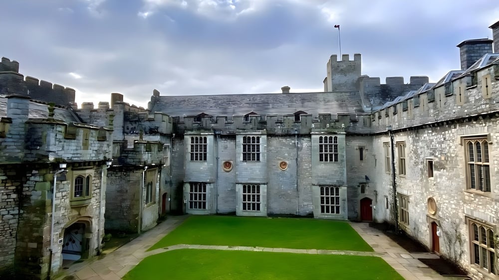 Das mittelalterliche Schloss des UWC Atlantic College mit Steinmauern, Türmen und einem grasbewachsenen Innenhof vor einem bewölkten Himmel.