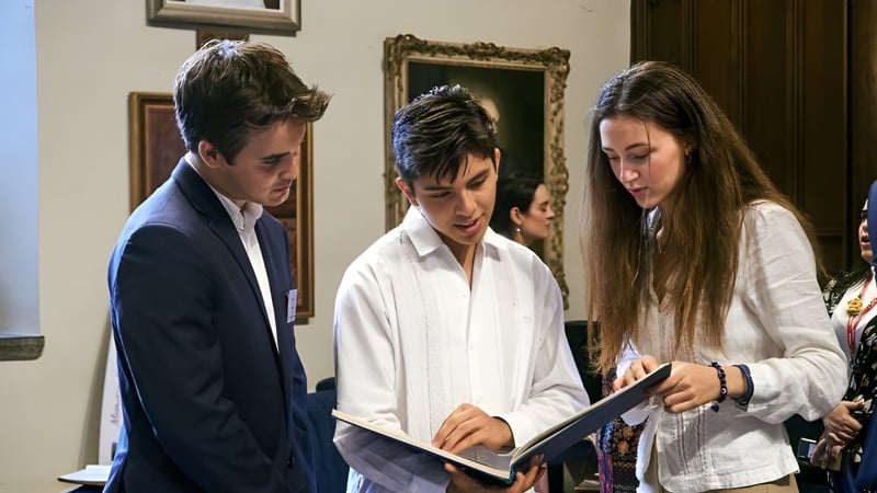 Zwei Schüler und eine Schülerin des UWC Atlantic College prüfen gemeinsam ein Dokument vor Kunstwerken.