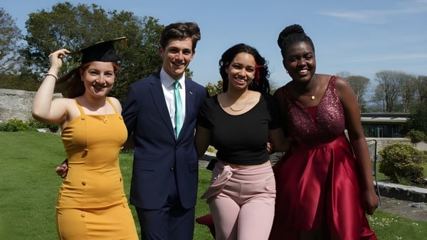 Vier Personen stehen zusammen im Freien auf dem Campus des UWC Atlantic College mit Bäumen und klarem Himmel im Hintergrund.