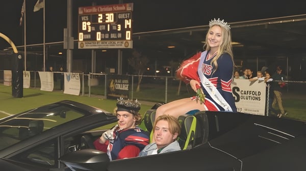 Eine Frau mit Krone und Schärpe steht neben einem Auto vor einer Anzeigetafel auf dem Campus der Vacaville Christian School.