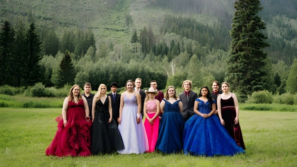 Eine Gruppe junger Schülerinnen in bunten Kleidern steht gemeinsam in der bewaldeten Berglandschaft auf dem Gelände der Valemount Secondary School.