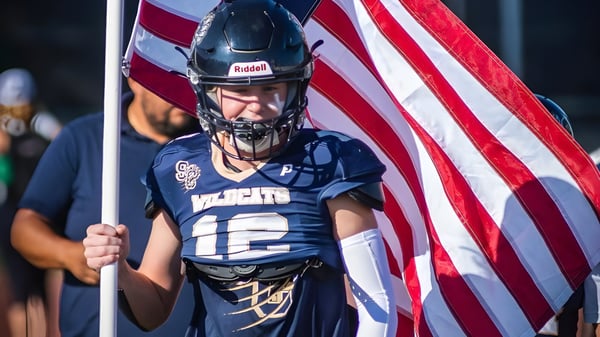 Ein Footballspieler der Valencia High School hält eine amerikanische Flagge vor einer Stadionkulisse.