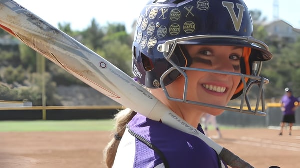 Eine junge Softballspielerin steht auf dem Baseballfeld der Valencia High School mit Wald im Hintergrund.