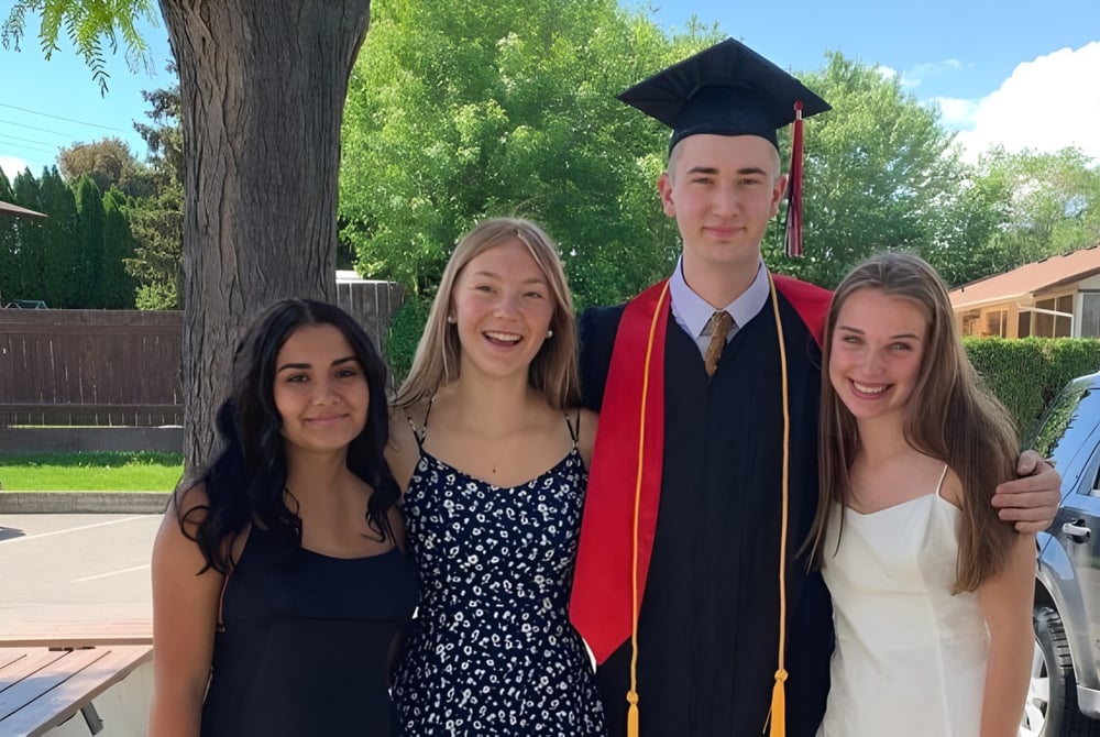 Eine Gruppe von Schülern der Valleyview Secondary School mit einem Absolventen in Robe steht draußen vor Bäumen und Gebäuden.