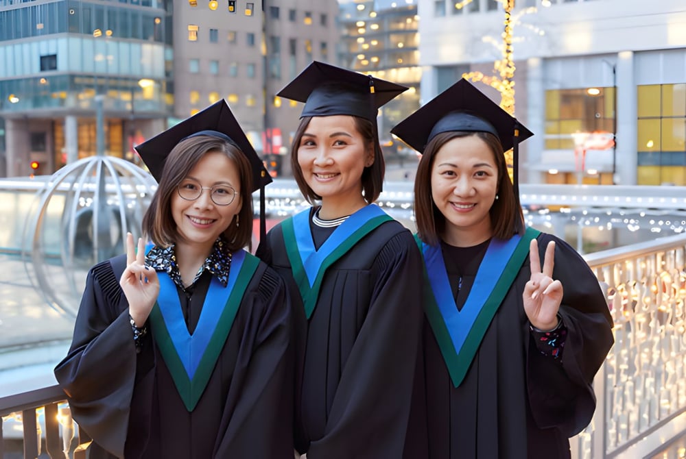 Drei Absolventinnen des Vancouver Community College stehen vor der Skyline einer modernen Stadt.