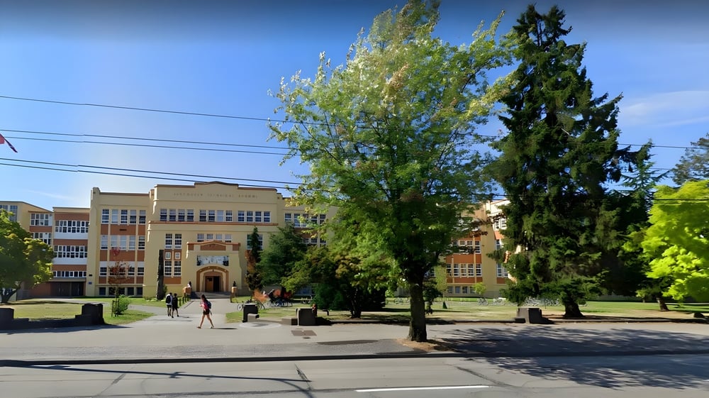 Der Campus der Vancouver Technical Secondary School zeigt große Bäume vor mehrstöckigen Schulgebäuden unter klarem Himmel.