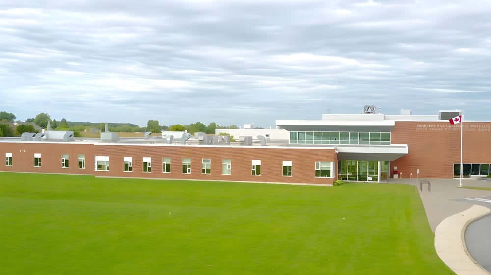 Das mehrstöckige Backsteingebäude mit großen Fenstern der Vankleek Hill Collegiate Institute steht auf einer Grasfläche umgeben von Bäumen.