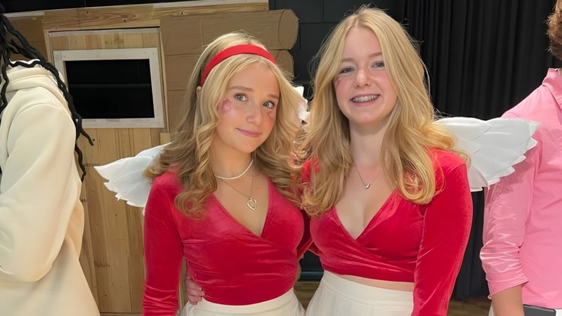 Zwei Schülerinnen des Vankleek Hill Collegiate Institute tragen rote Samtoberteile und stehen vor Kleidungsgestellen und einer Holzkonstruktion.