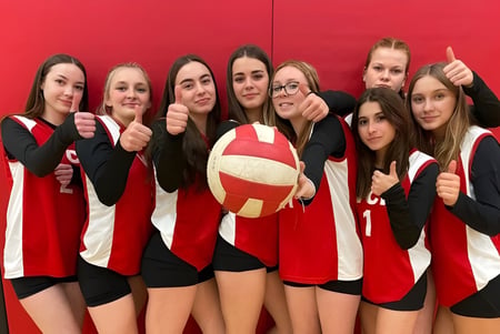 Eine Gruppe junger weiblicher Schüler im Volleyball-Trikot posiert mit Ball vor rotem Hintergrund auf dem Campus der Vankleek Hill Collegiate Institute.