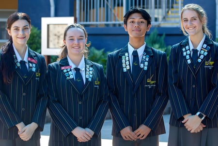 Vier Studentinnen in akademischer Kleidung stehen vor einem Gebäude mit blauer Fassade auf dem Campus des Varsity College.