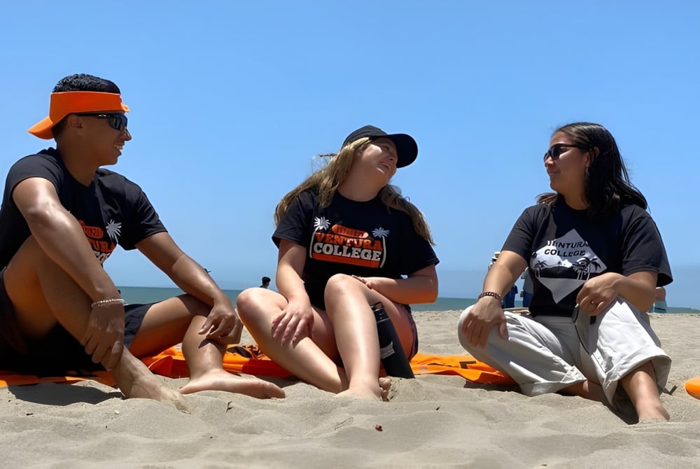 Drei Personen sitzen am Strand unter blauem Himmel auf dem Campus des Ventura County Community College District.