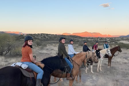 Schüler der Verde Valley School reiten auf Pferden durch eine landschaftlich reizvolle Wüstenlandschaft mit Bergen im Hintergrund.