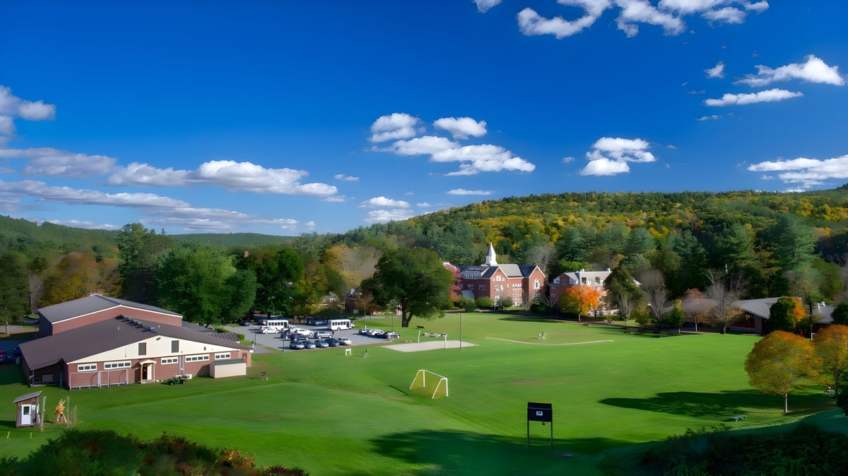 Ein grüner Golfplatz mit herbstlich buntem Laub und einem Dorf mit Kirchturm im Hintergrund auf dem Campus der Vermont Academy.