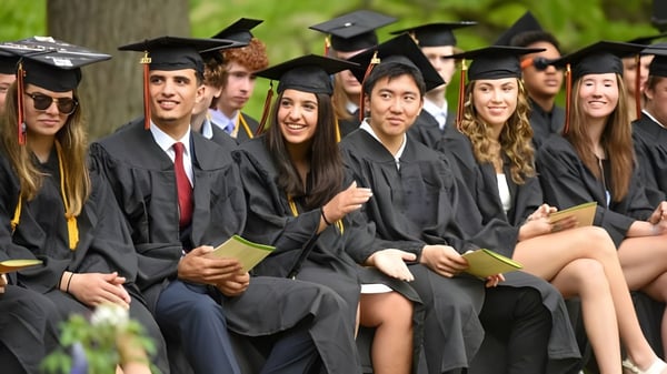 Eine Gruppe von Absolventinnen und Absolventen der Vermont Academy sitzt in akademischer Kleidung im Freien vor Bäumen.