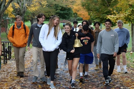 Eine Gruppe Schülerinnen und Schüler der Vermont Academy geht gemeinsam auf einem Weg mit buntem Herbstlaub.