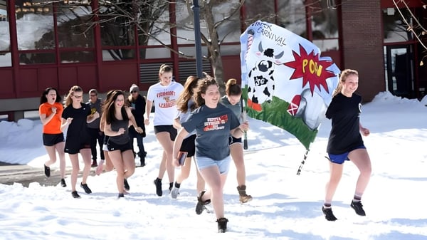 Eine Gruppe von Schülerinnen der Vermont Academy trägt ein großes buntes Banner durch eine verschneite Außenanlage.