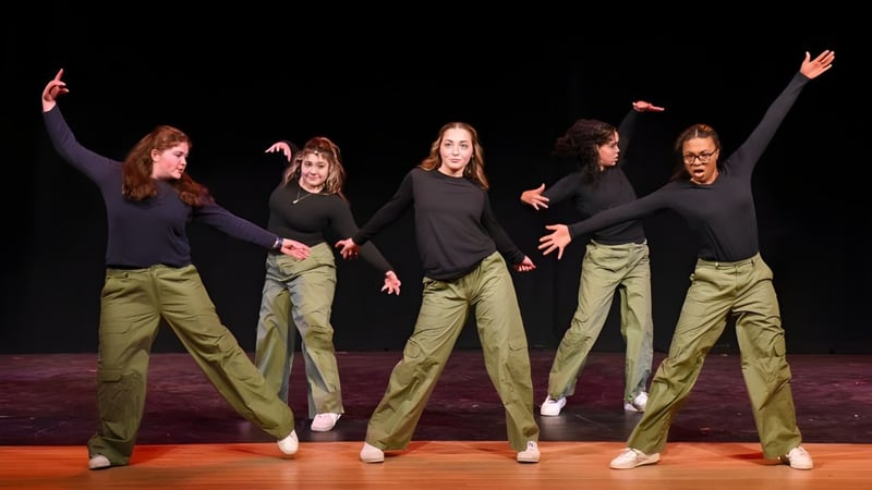 Eine Gruppe von fünf Schülerinnen der Vermont Academy führt eine synchronisierte Tanzaufführung auf einer Bühne mit dunklem Hintergrund auf.