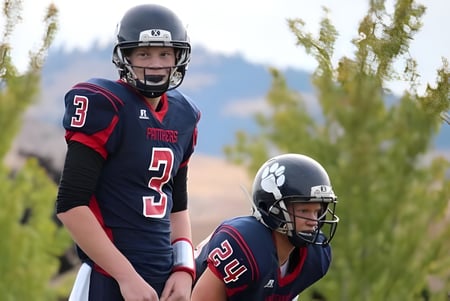 Zwei Footballspieler in Uniform stehen auf einem Feld mit hohem Gras vor Bäumen auf dem Gelände der Vernon Secondary School.