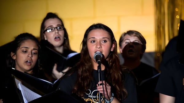 Schüler der Vernon Township High School singen gemeinsam auf einer Bühne mit gelbem Hintergrund.
