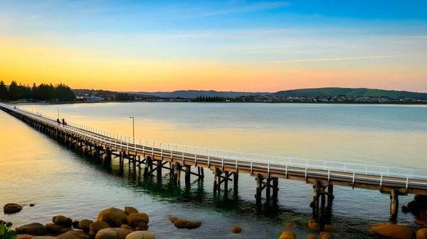 Ein langer Holzsteg erstreckt sich auf dem Gelände der Victor Harbor High School über einen ruhigen See mit grünen Hügeln im Hintergrund.