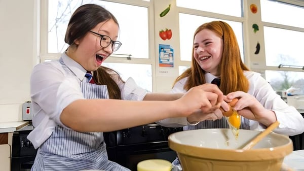 Zwei Schülerinnen des Victoria College Belfast arbeiten gemeinsam und lachen in einer Schulküche.