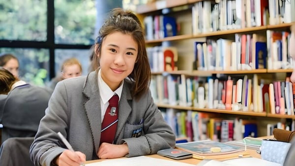 Eine Schülerin des Victoria College Belfast sitzt an einem Tisch in der Bibliothek zwischen Bücherregalen.