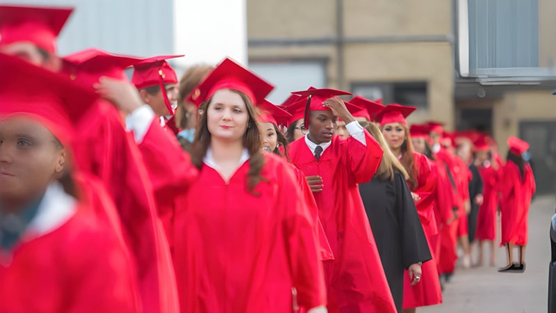 Eine Gruppe von Absolventinnen und Absolventen der Victoria High School steht in roten Talaren vor einem Schulgebäude.