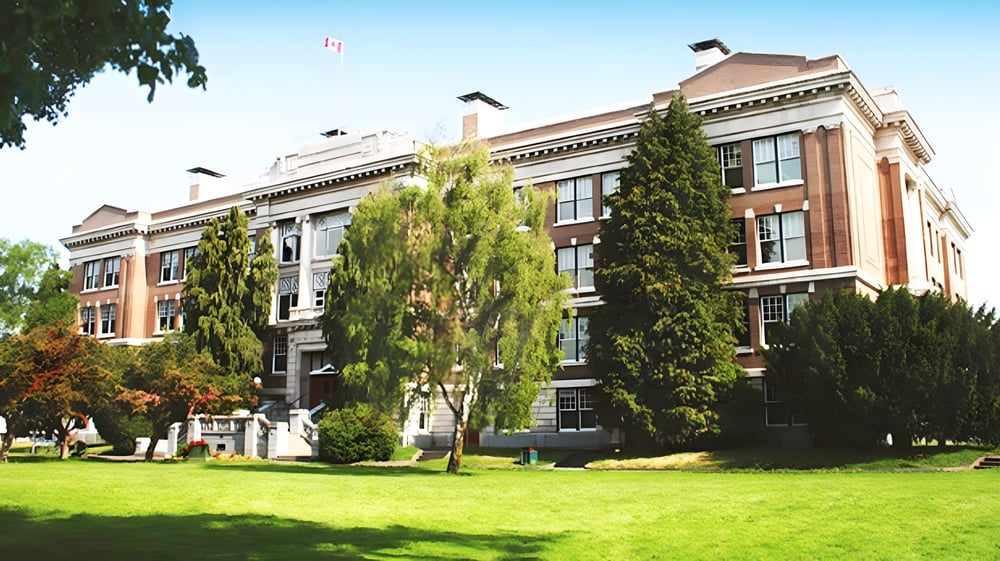 Das historische Backsteingebäude der Victoria High School steht auf einem grünen Rasen mit umgebenen Bäumen.