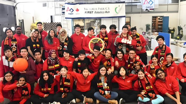 Eine große Gruppe von Schülerinnen und Schülern des Victoria Park Collegiate Institute posiert in roten Sportjacken in einer Sporthalle.
