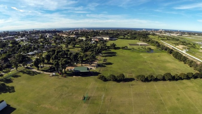 Ein weites grünes Feld mit einzelnen Bäumen vor einer Stadtkulisse auf dem Gelände der Victoria Park High School.