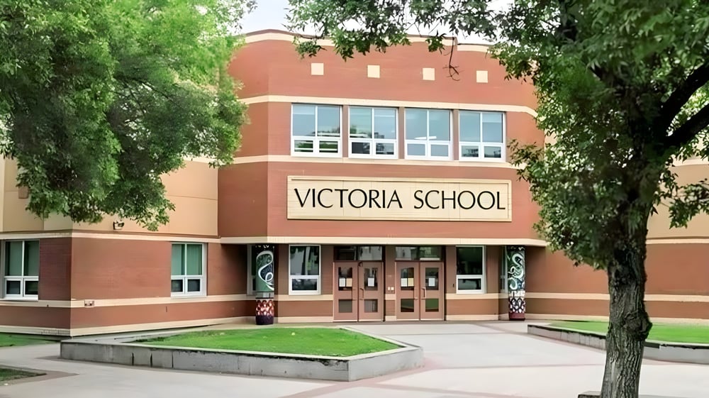 Das Backsteingebäude der Victoria School of the Arts ist von grünen Bäumen und einer Rasenfläche umgeben.