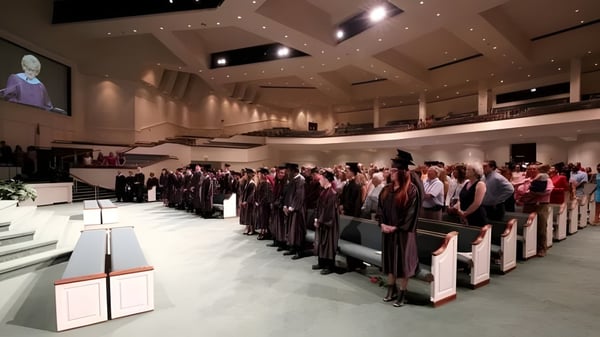Schüler der Victory Christian Academy sitzen in einem großen Saal bei der Abschlussfeier mit Bühne und Rednerpult im Hintergrund.