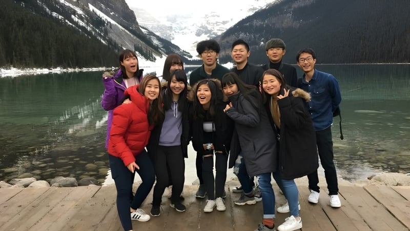 Eine Gruppe von Menschen steht bei der Viking School auf einem Holzsteg vor einer Berglandschaft mit See.