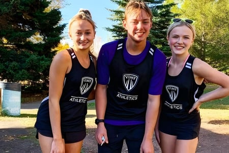 Drei Schüler der Vimy Ridge Academy stehen zusammen im Freien in sportlichen Teamuniformen vor einem parkähnlichen Hintergrund.