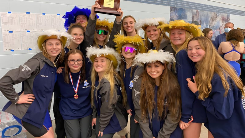 Eine Gruppe Schülerinnen des Virginia Beach City Public School District posiert in bunten Perücken und Kostümen vor Schulpostern.