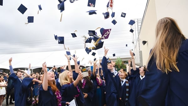 Absolventen in blauen Talaren der Vistamar School werfen ihre Hüte während der Abschlussfeier in die Luft.