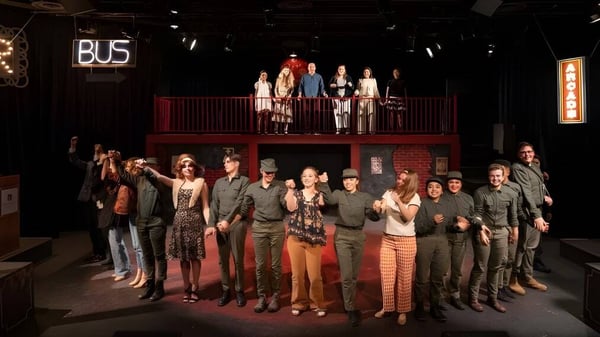 Schüler der Vistamar School versammeln sich auf der Bühne und im Vordergrund eines theatralisch beleuchteten Raums mit sichtbarem BUS-Schild im Hintergrund.