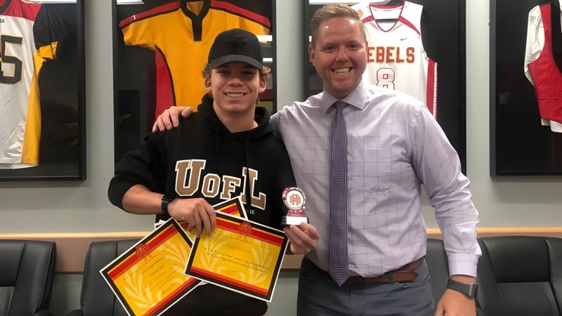 Ein Mann und eine Frau stehen in einer sportlichen Umgebung mit Sporttrikots im Hintergrund auf dem Campus der W.R Myers High School.