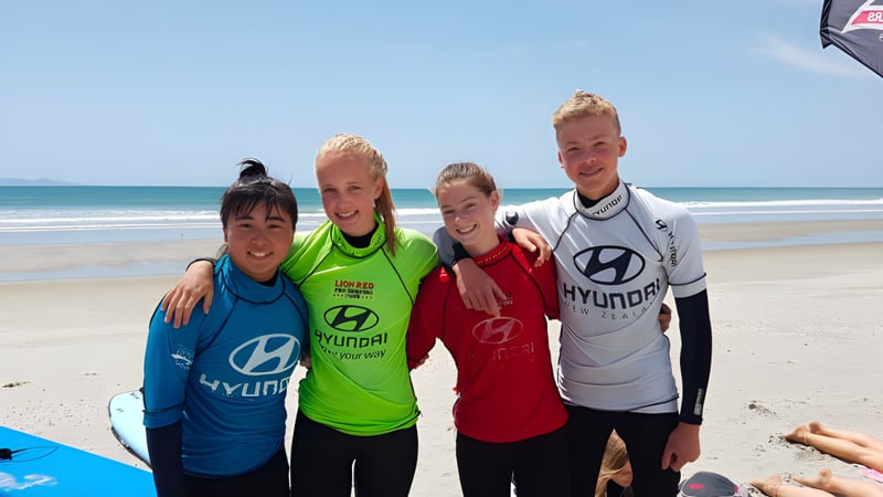 Eine Gruppe von vier Schülerinnen und Schülern steht am Strand mit dem Ozean im Hintergrund auf dem Gelände von Waihi College.