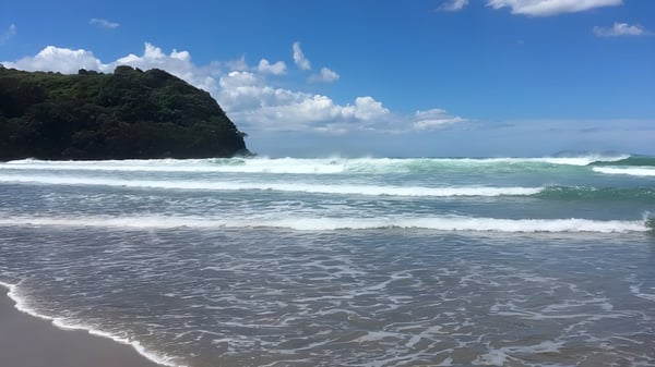 Eine Strandlandschaft mit Wellen, Felsen und blauem Himmel nahe dem Waihi College.