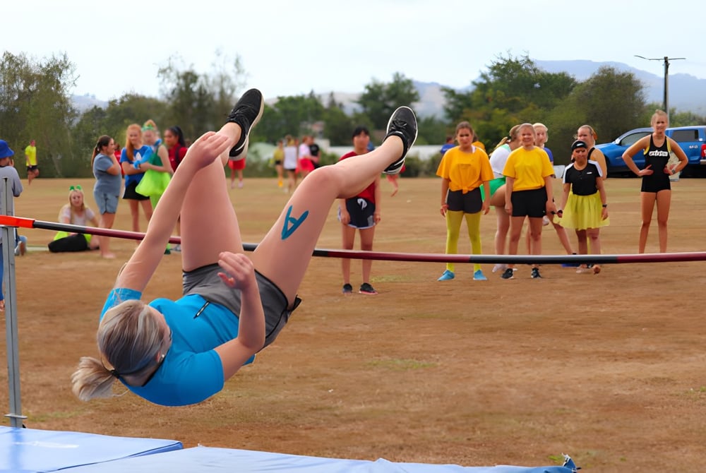 Eine Schülerin führt eine Gymnastikübung auf einer Matte auf dem Außengelände des Waihi College vor einer Gruppe von Zuschauern aus.