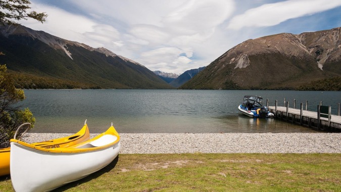 Ein ruhiger See mit einem weißen und gelben Kanu im Vordergrund vor der Kulisse von Bergen auf dem Gelände des Waimea College.