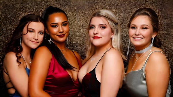 Vier Frauen mit unterschiedlichen Erscheinungsbildern posieren gemeinsam vor goldenem Hintergrund auf dem Campus des Waitakere College.