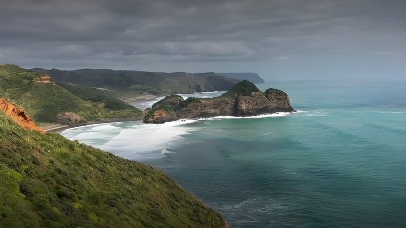 Felsige Küstenlandschaft mit türkisfarbenem Wasser und dichter Vegetation nahe Waitakere College.
