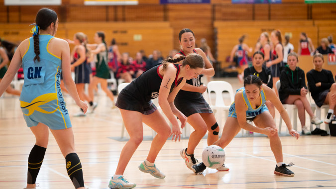 Athletinnen der Waitaki Girls’ High School nehmen an einem Hallensportwettkampf teil, im Hintergrund sind Zuschauer zu sehen.