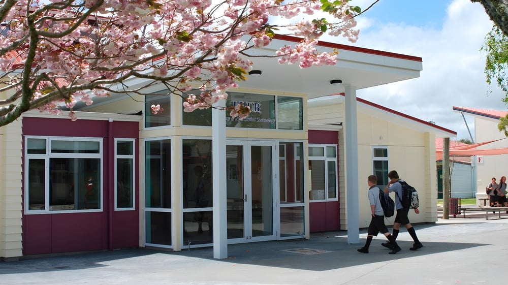 Ein modernes Gebäude mit Glaseingang und einem blühenden Kirschbaum im Vordergrund auf dem Campus des Waiuku College.
