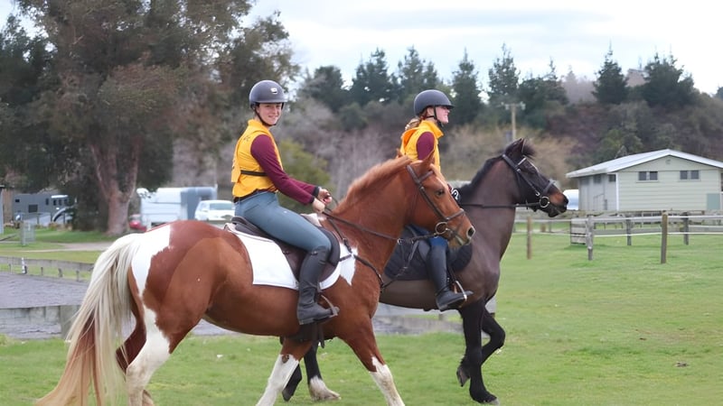 Zwei Personen reiten Pferde auf einem grasbewachsenen Feld auf dem Campus des Waiuku College.