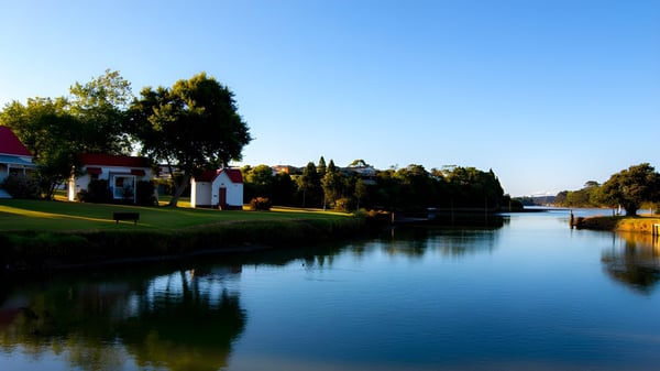 Ein ruhiger Wasserweg mit bunten Gebäuden und Bäumen spiegelt sich im Wasser auf dem Gelände des Waiuku College.